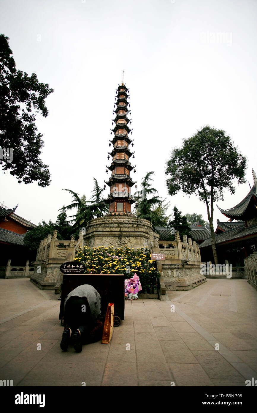 Persona cinese inginocchiato in preghiera e adorazione davanti a una pagoda all'interno di un monastero/tempio Foto Stock