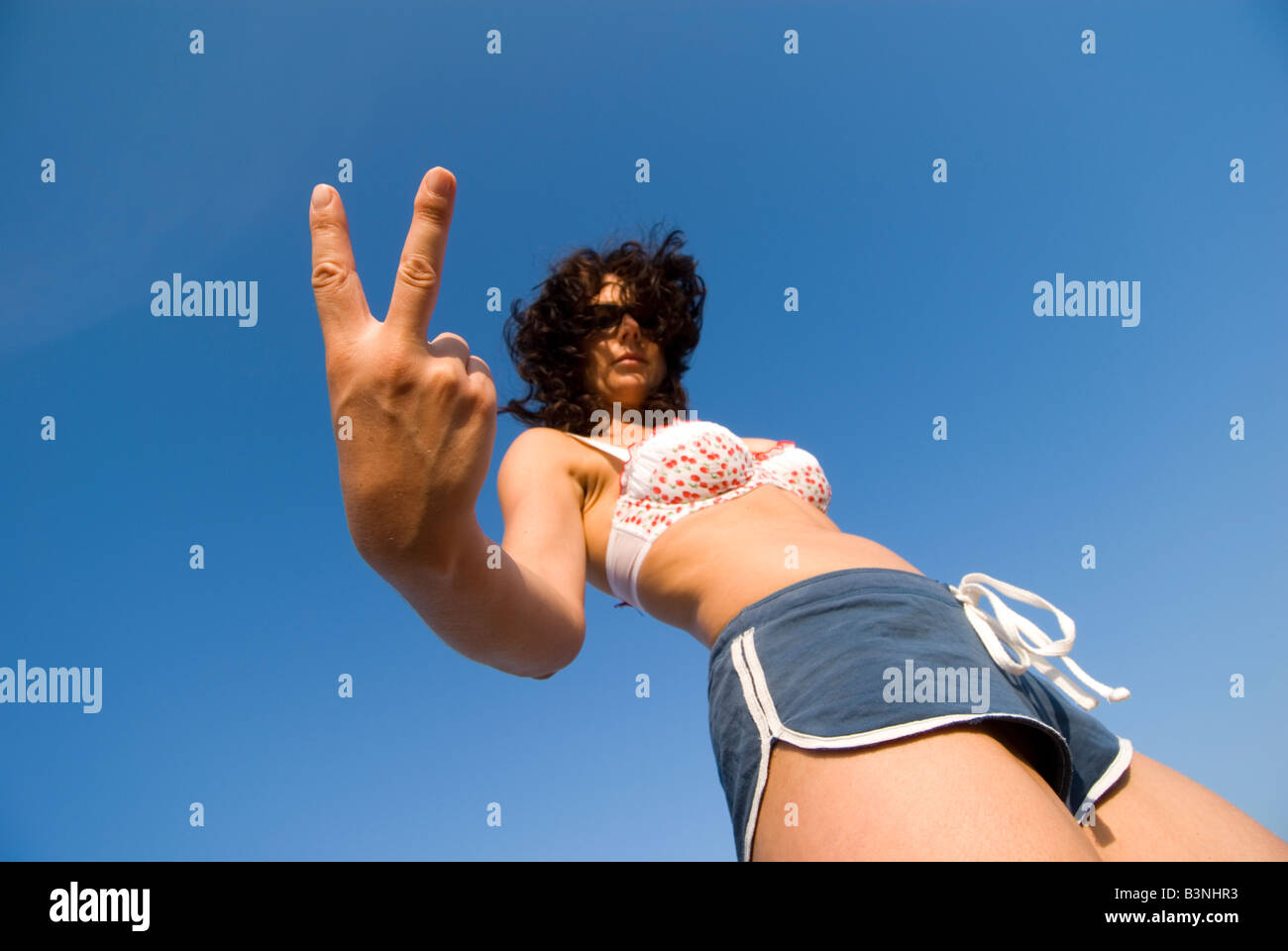 Modello rilasciato femmina formando un abusivo segno V vestito di beachwear basso angolo la messa a fuoco a portata di mano Foto Stock