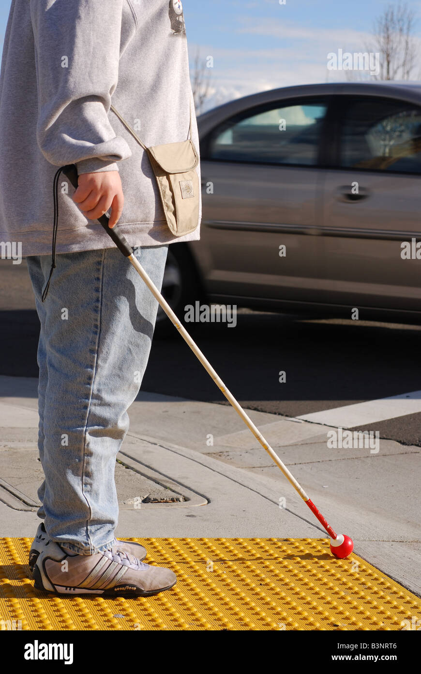 Blind donna in piedi sulla piattaforma crosswalk come una velocità di auto da Foto Stock