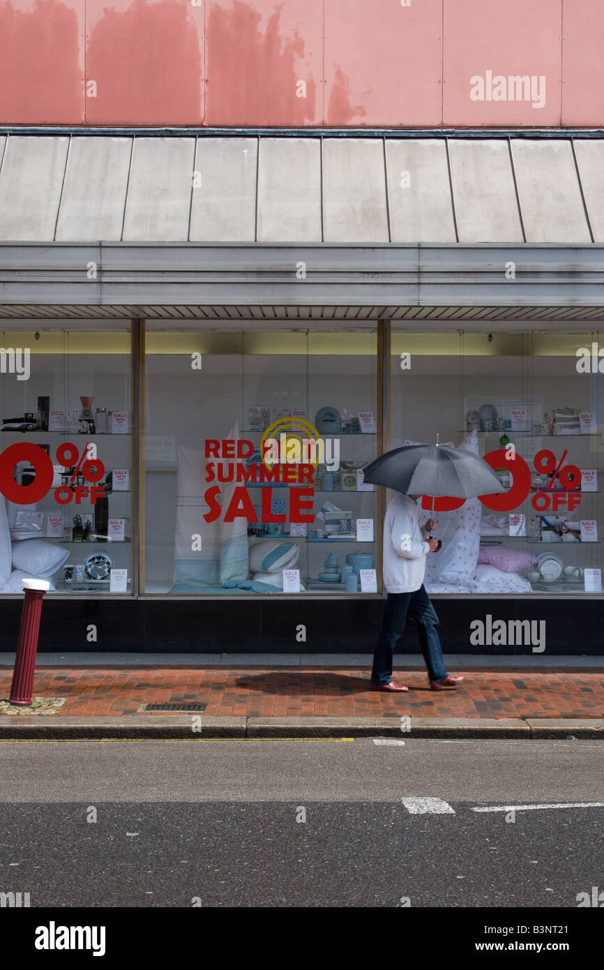 Uomo con ombrello passeggiate passato shop sotto la pioggia pubblicità un Red Hot Summer Sale Foto Stock