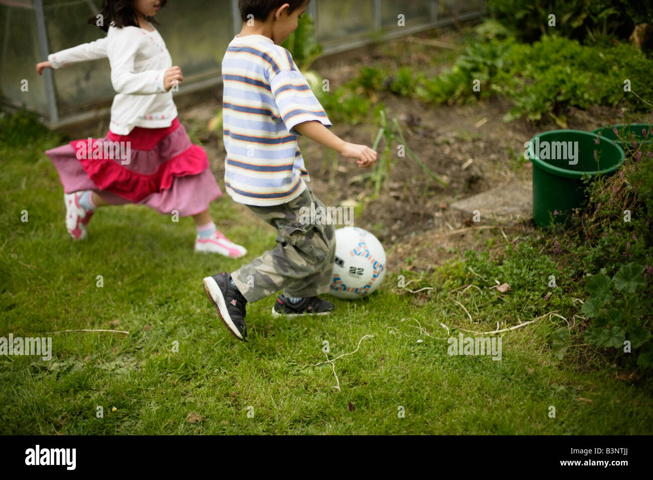 Ragazzo di età compresa tra sei e sorella cinque giocare a calcio calci palla in patch vegetale Foto Stock