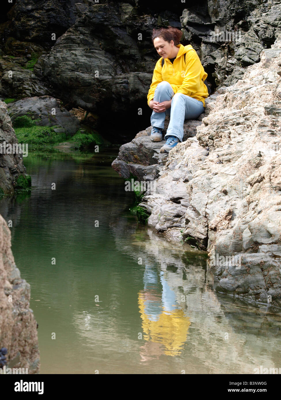 Brunette donna che indossa jeans seduto su una roccia che guarda nel flusso stretto. Foto Stock