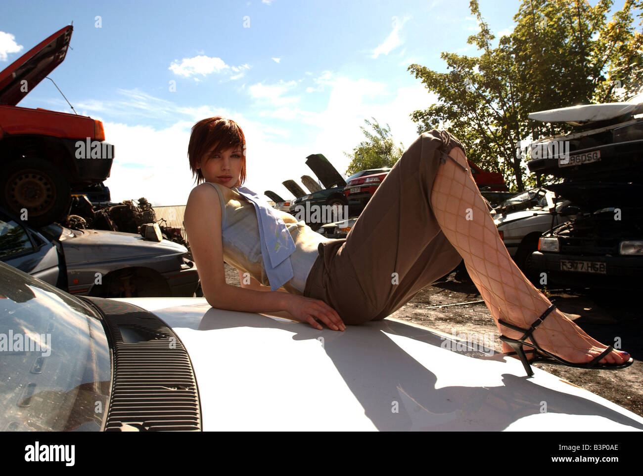 Urban Chic moda Ottobre 2001 Modello Lorna Paisley indossando brown contro cortocircuiti e collant da donna con tacco alto scarpe in posa sulla parte superiore delle automobili presso un cantiere di scarto Foto Stock