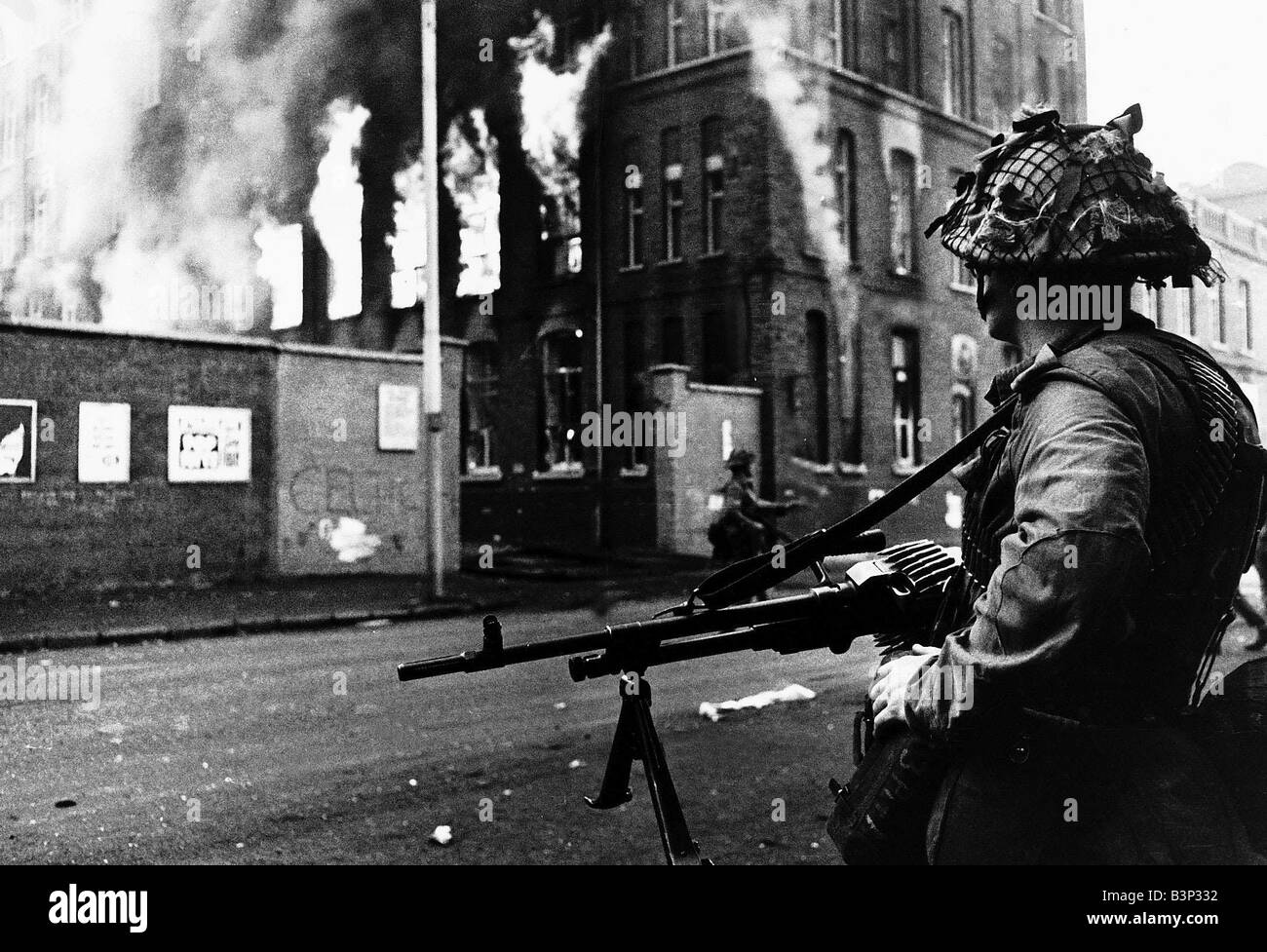 Disordini a Belfast le truppe britanniche di guardia a Falls Road Belfast soldato in piedi con una pistola guardando un edificio in fiamme Foto Stock