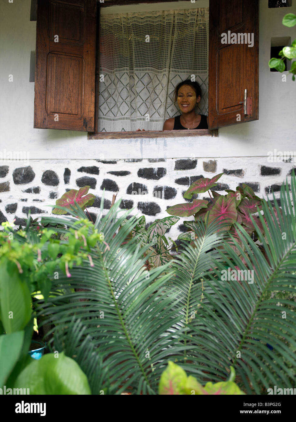 Madagascar settentrionale, un malgascio donna guarda fuori dalla finestra della sua attraente casa a Ramena, un villaggio di pescatori che si trova a breve distanza da Antsiranana, più comunemente noto come Diego.Ha il viso coperto con un impasto costituito da polvere di legno e semi di un albero speciale per evitare scottature. Questa forma di protezione dal sole è molto comune tra le donne che lavorano nelle risaie tutto il giorno. Foto Stock