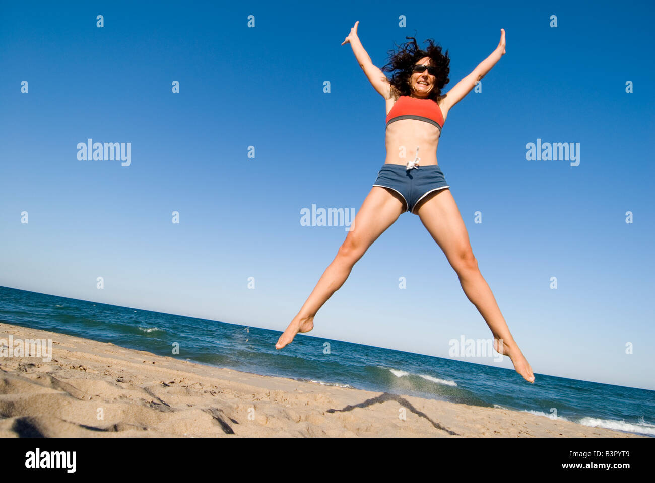 Modello rilasciato giovane donna stella facendo saltare su di una spiaggia di sabbia contro un cielo blu chiaro. El Saler. Valencia Spagna Foto Stock