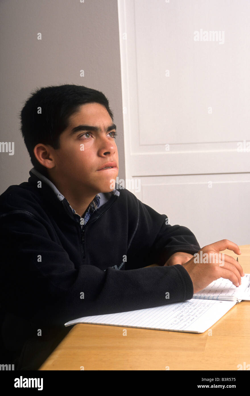 Ispanico pre-teen boy pensa disco mentre si fanno i compiti a tavola in casa sua. Foto Stock