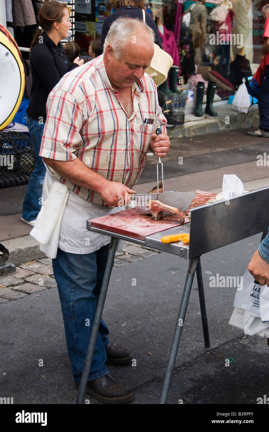 Un macellaio che usa un sfaldatore di carne per preparare un taglio di maiale in un mercato di strada francese, nella città di Portbail, Normandia, Francia Foto Stock