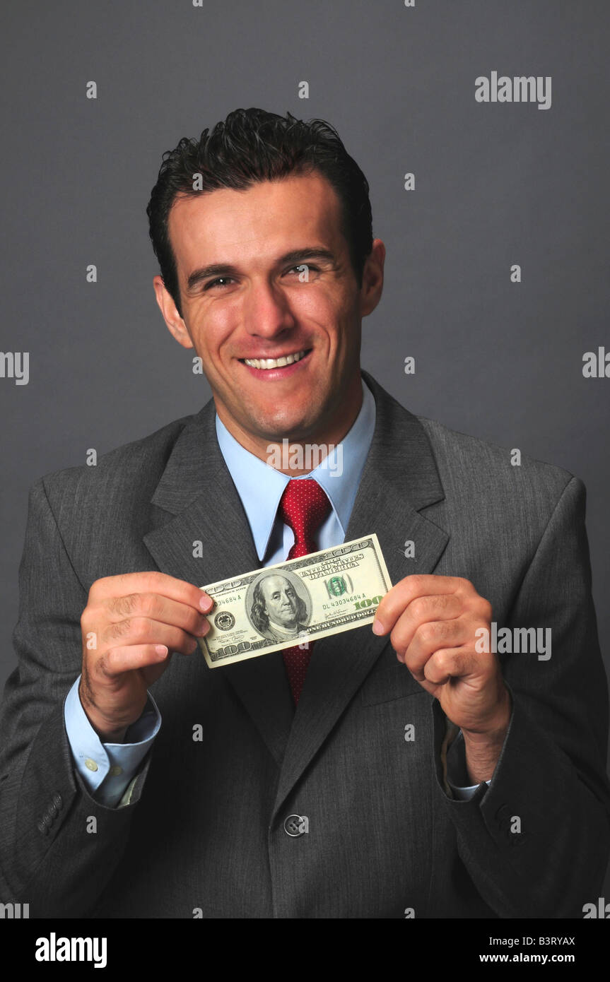 Imprenditore sorridente tenendo un centinaio di dollari di fronte a uno sfondo grigio Foto Stock