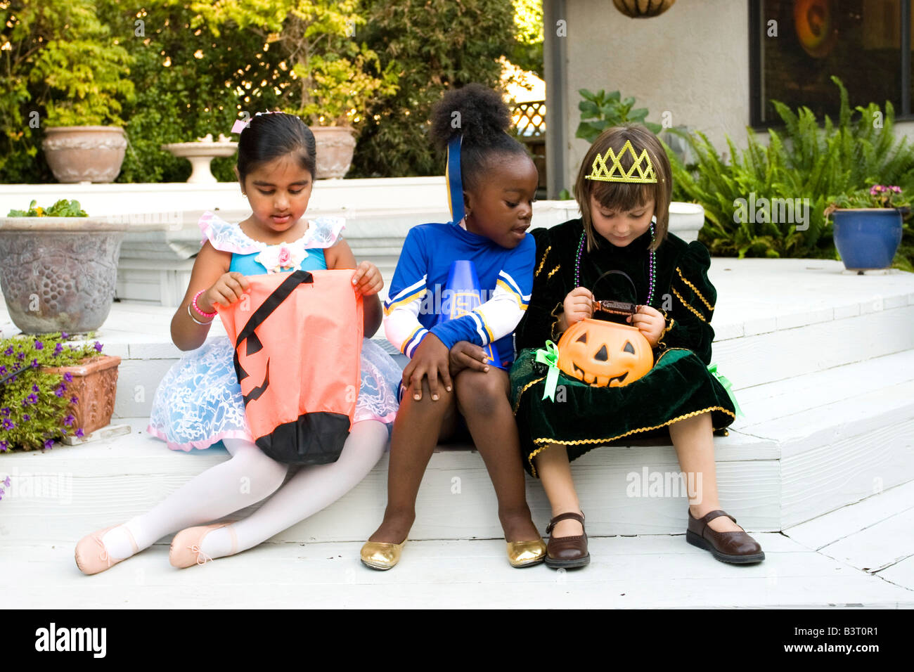 Bambine vestite come ballerina e principessa controllare i loro Halloween goodies mentre la cheerleader analizza il princess' borsa Foto Stock