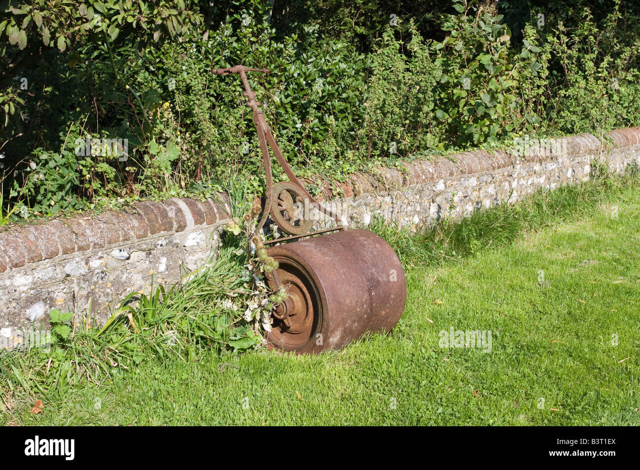 Rullo da giardino in appoggio contro un basso muro di pietra Foto Stock