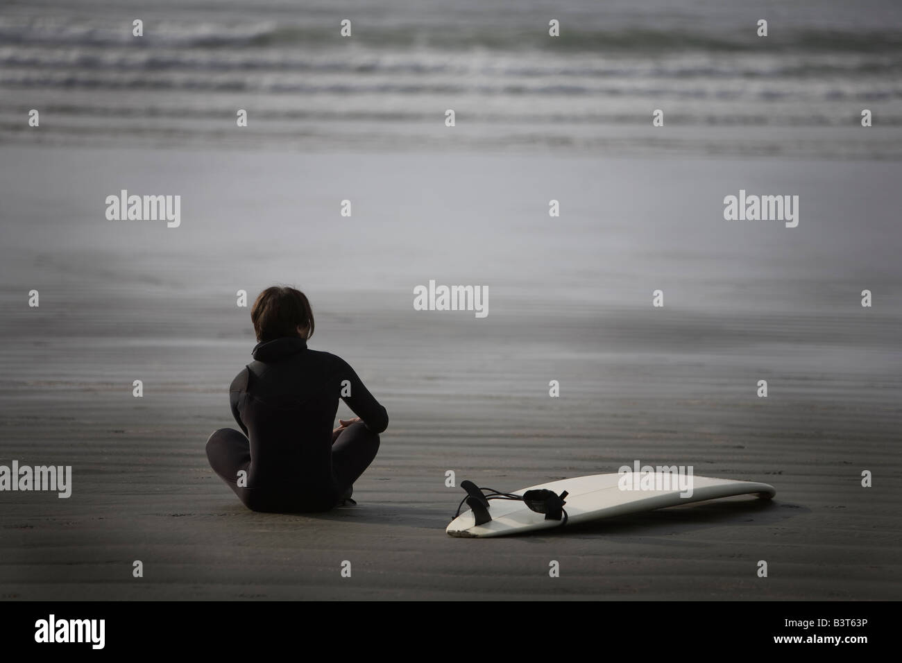 Surfer seduto sulla spiaggia, Cox baia vicino a Tofino, British Columbia, Canada Foto Stock