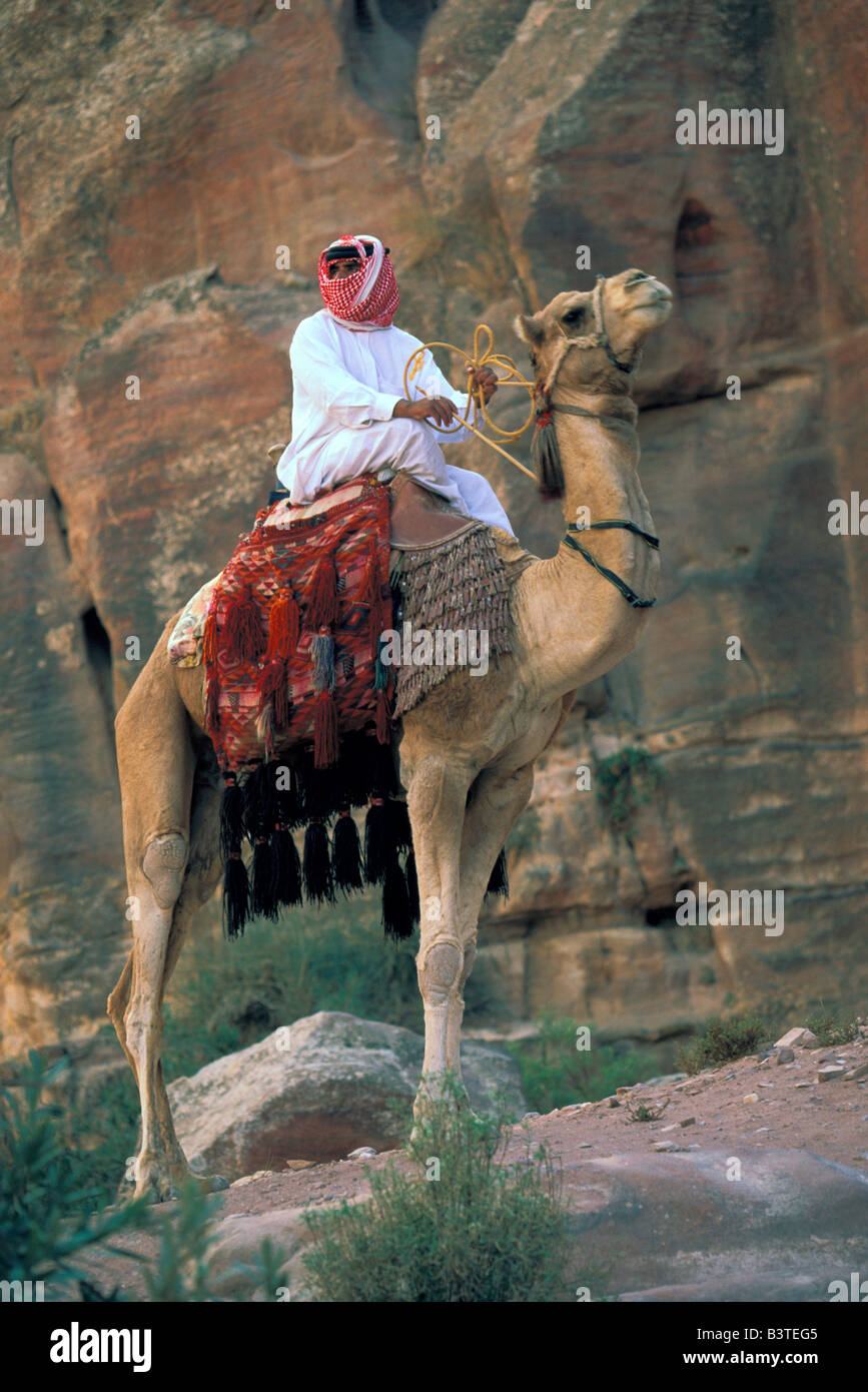Asia, Giordania Petra. Uomo locale a dorso di cammello vicino rovine. Foto Stock