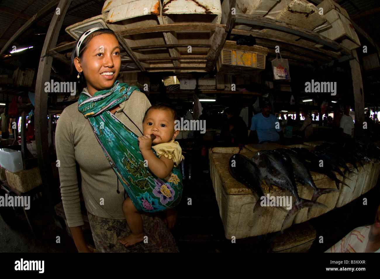 Una donna che porta in sé il figlio in una imbracatura nel mercato del pesce a Denpasar Bali Indonesia Foto Stock