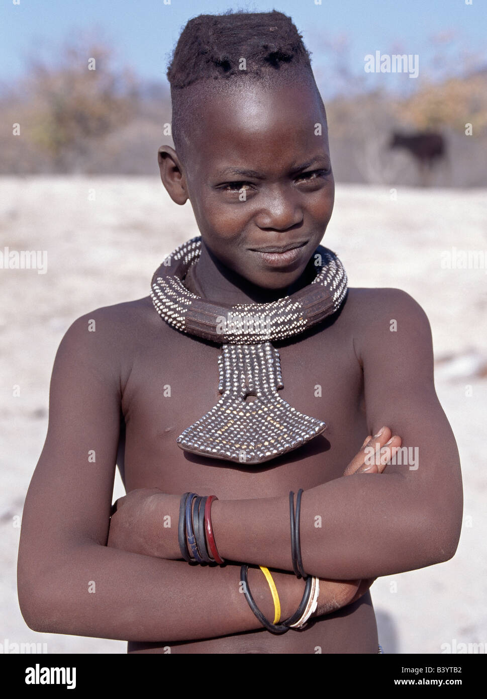 La Namibia, il Kaokoland, Empembe. Una giovane ragazza Himba ha i capelli in due trecce, il consueto stile di giovani ragazze fino all'adolescenza. La sua grande, bianco rotondo-collana di perle, chiamato ombwari, è indossato da entrambi i sessi. Il suo altro ornamento del collo è costituito da perline di metallo supportato sul cuoio. Gli Himba sono Herero-parlando Bantu nomadi che vivono nel duro, secco ma fortemente bellissimo paesaggio del nord-ovest remota Namibia. Foto Stock