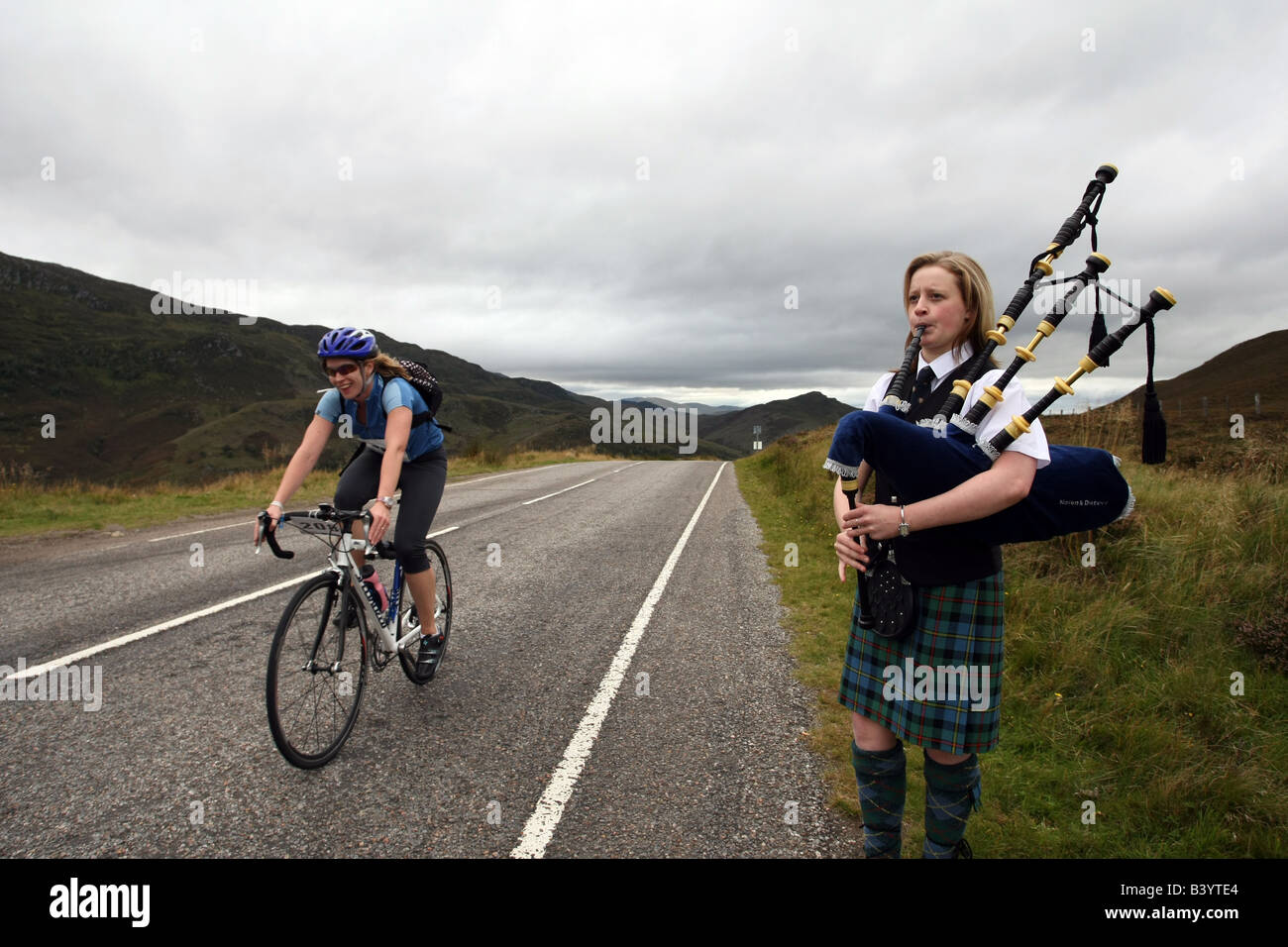 Ciclista sulla bici da corsa passa un piper sulla B862, Great Glen modo attorno a Loch Ness, Highlands scozzesi, Scotland, Regno Unito Foto Stock
