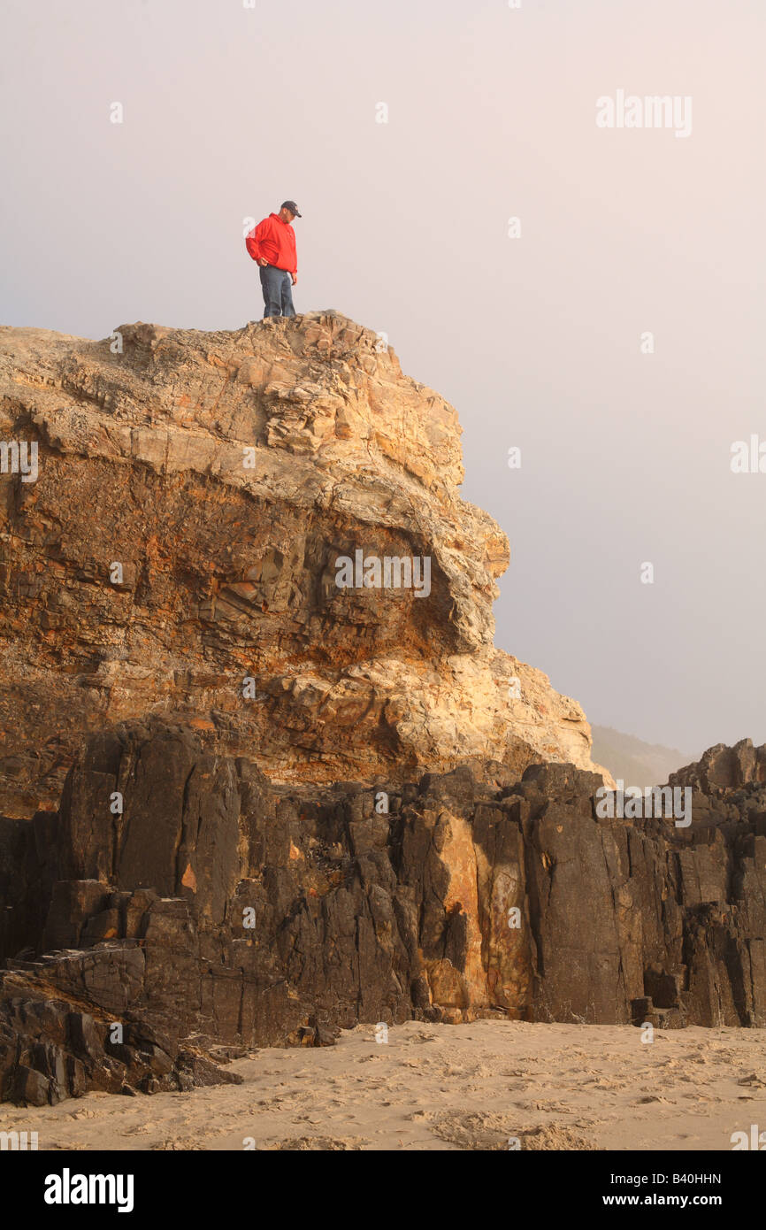 Uomo in piedi sulla cima di una scogliera che si affaccia sulla spiaggia Foto Stock