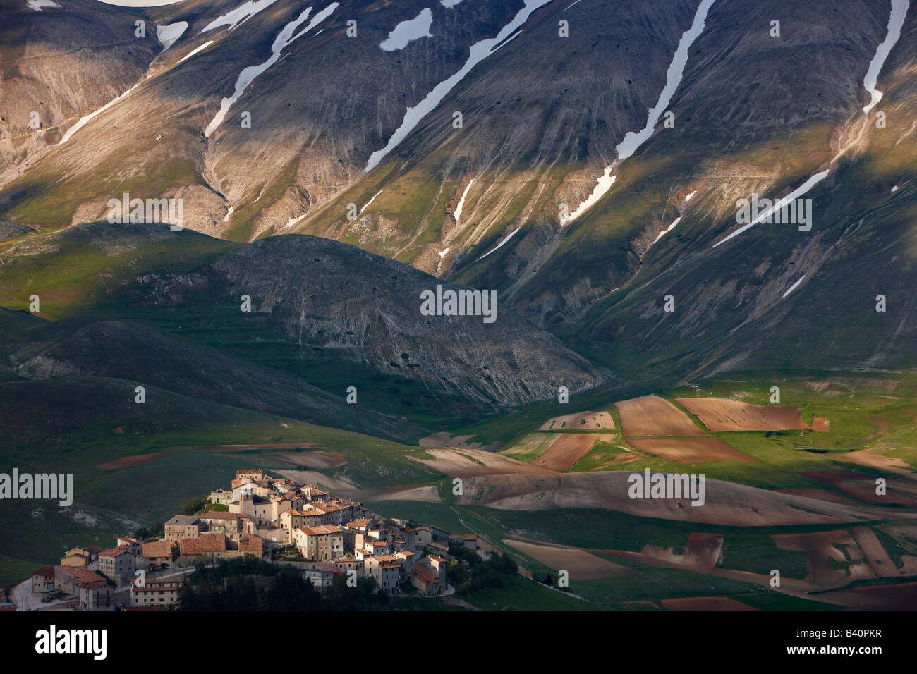 Il borgo di Castelluccio arroccato sopra il piano Grande con le montagne del Parco Nazionale dei Monti Sibillini, Umbria, Italia Foto Stock