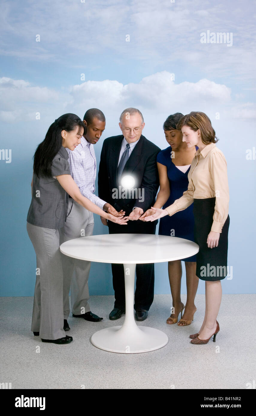 Il gruppo di cinque multi etnico stand di persone intorno al tavolo osservando floating incandescente fenomeno orb Foto Stock