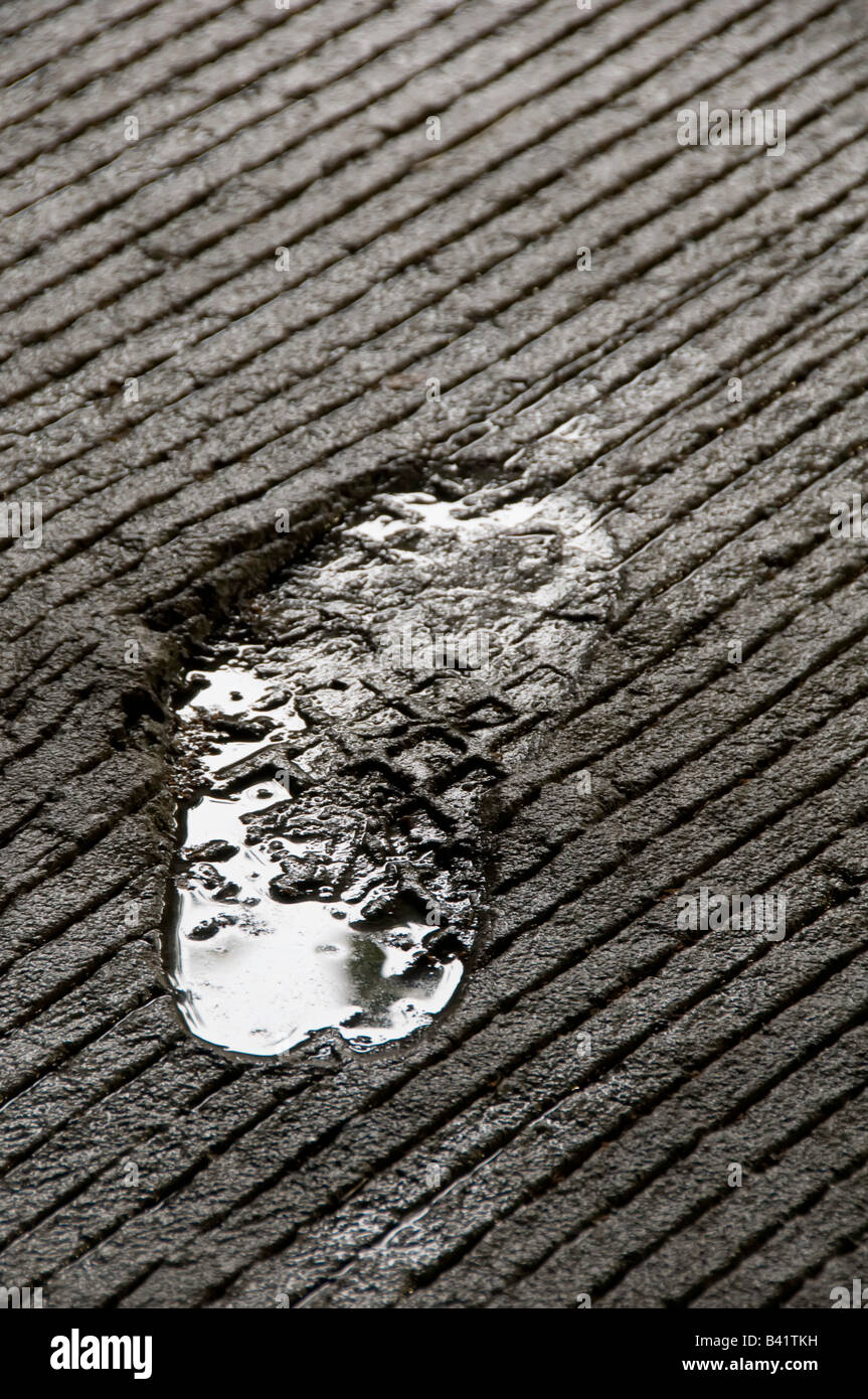 Sunken shoeprint con acqua piovana che riflette le nuvole impostato in calcestruzzo rigato pavimento del garage Foto Stock