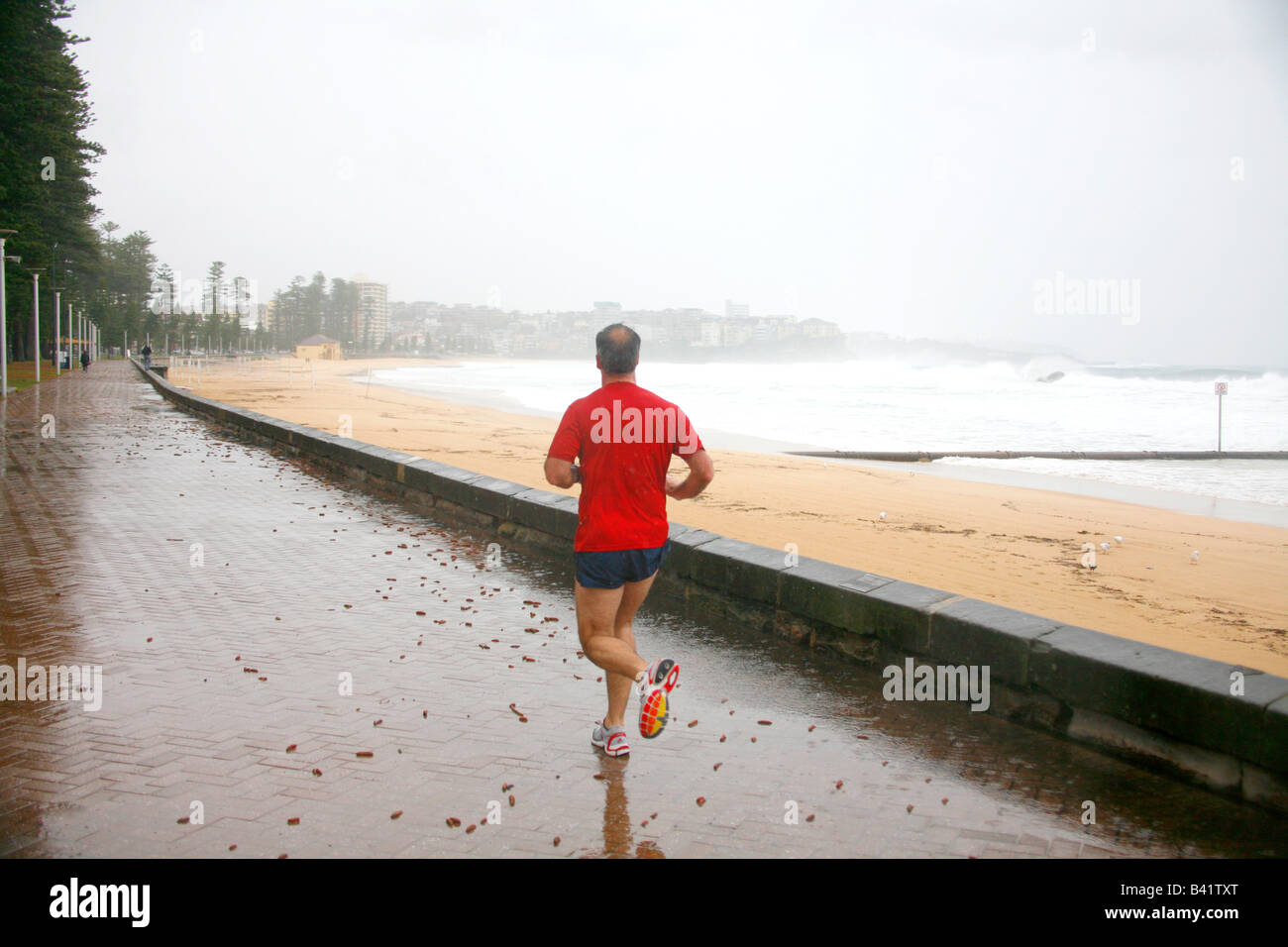 Un uomo in un rosso t shirt viene eseguito durante una tempesta in Manly Australia Foto Stock