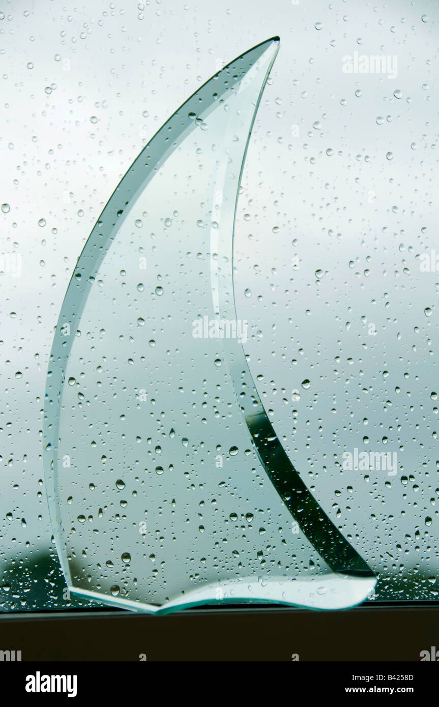 Pezzo curvo di vetro tagliato a forma di vela sulla mensola all'interno di una finestra di pioggia Foto Stock