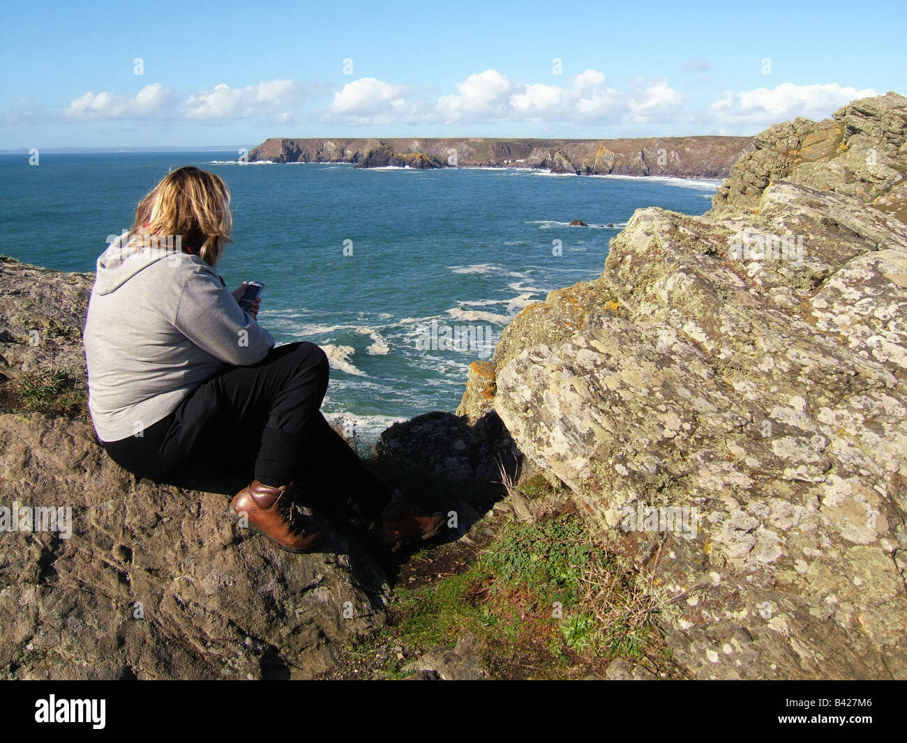Donna seduta sul bordo scogliera affacciato sul Cornish Coast a Kynance Cove La Lucertola Cornwall Inghilterra REGNO UNITO Foto Stock