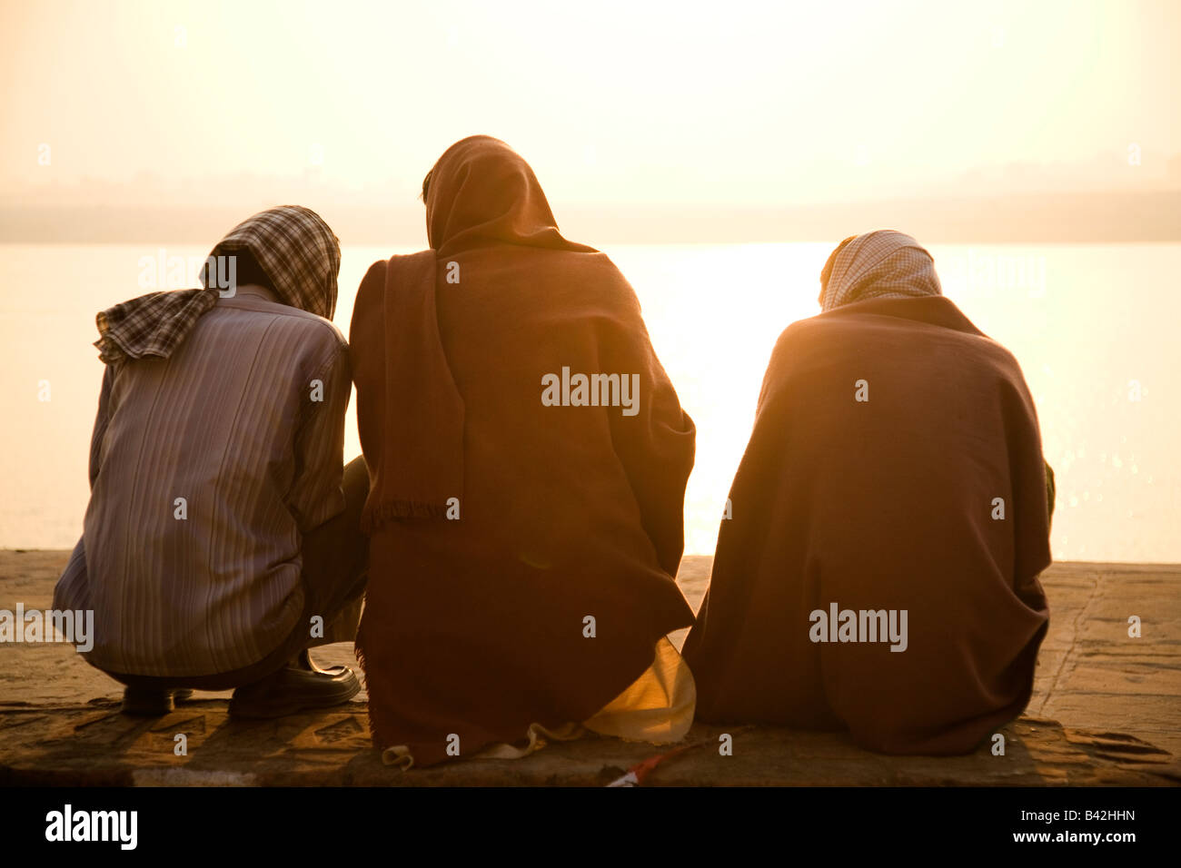 Sunrise di Varanasi (India). Tre uomini chat come il sole sorge sul fiume Ganga (il Gange). Foto Stock