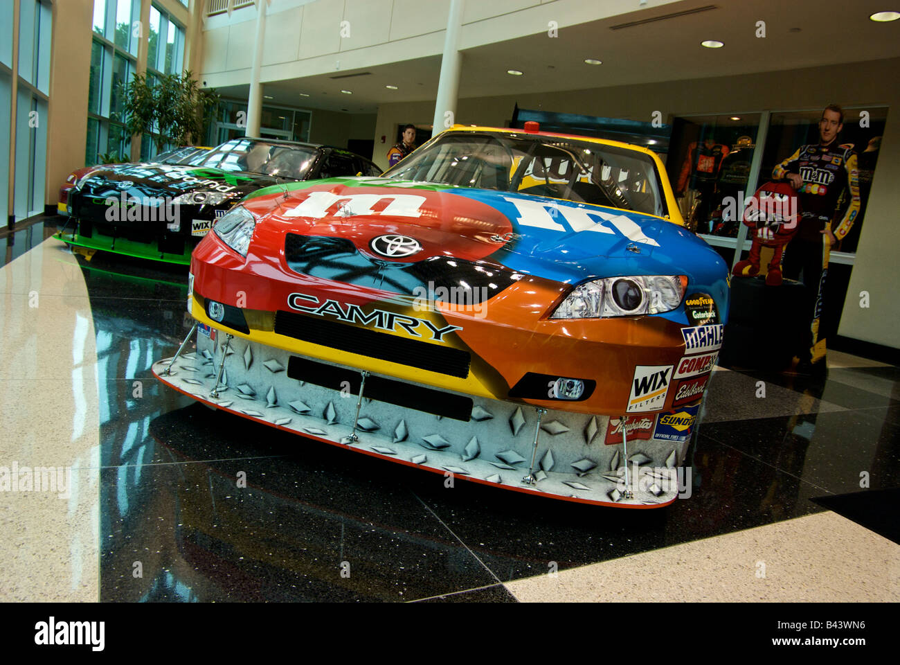Kyle Busch m&m Toyota Camry NASCAR Race Cars con sponsor le decalcomanie su display a Joe Gibbs Racing showroom Foto Stock