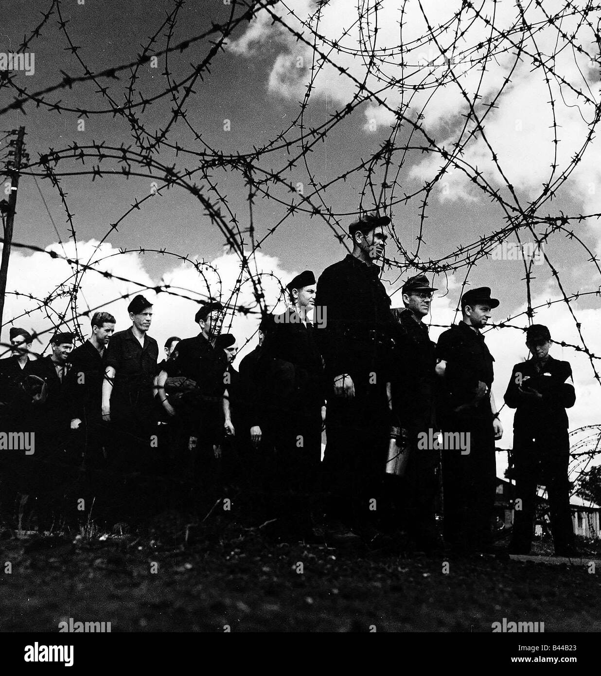 WW2 i prigionieri di guerra tedeschi in un campo di prigionia permanente per l'attenzione nelle loro divise dietro al filo spinato Foto Stock