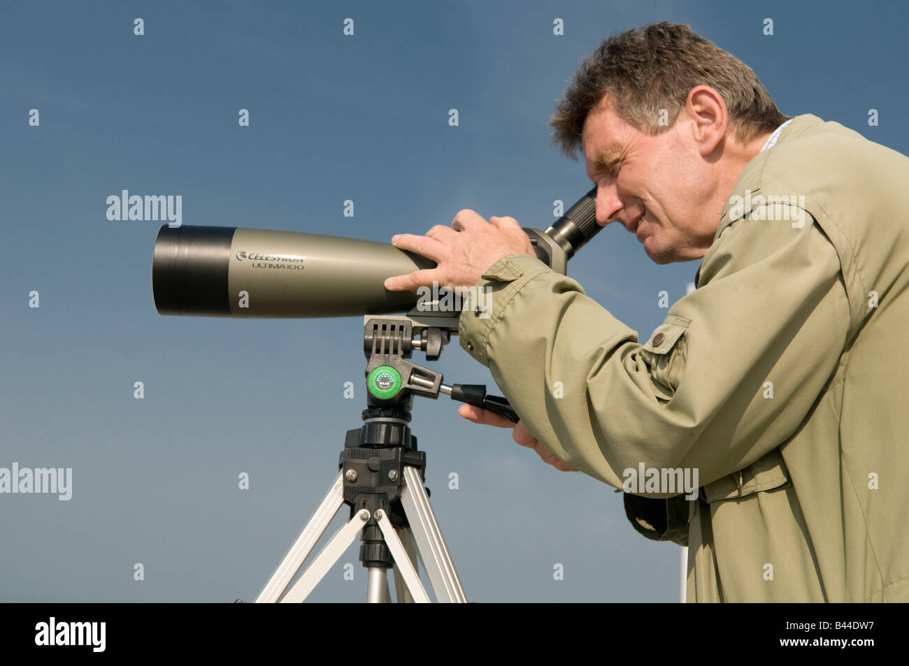 Uomo di mezza età ornitologo guardando gli uccelli attraverso un telescopio monoculare un treppiede mattinata estiva Wales UK, cielo blu Foto Stock