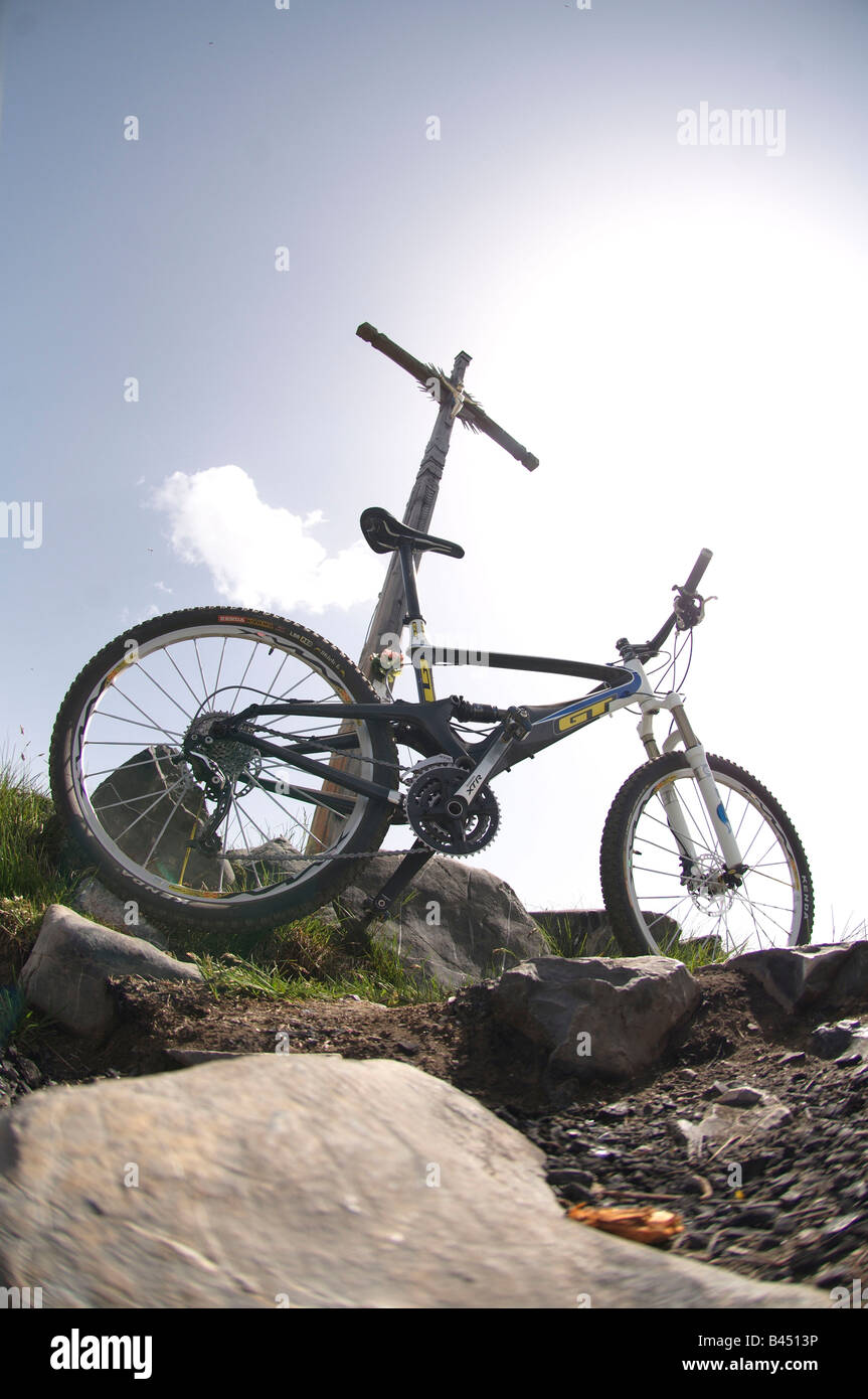 Mountain bike appoggiato contro una croce sopra Livigno, Italia. Foto Stock