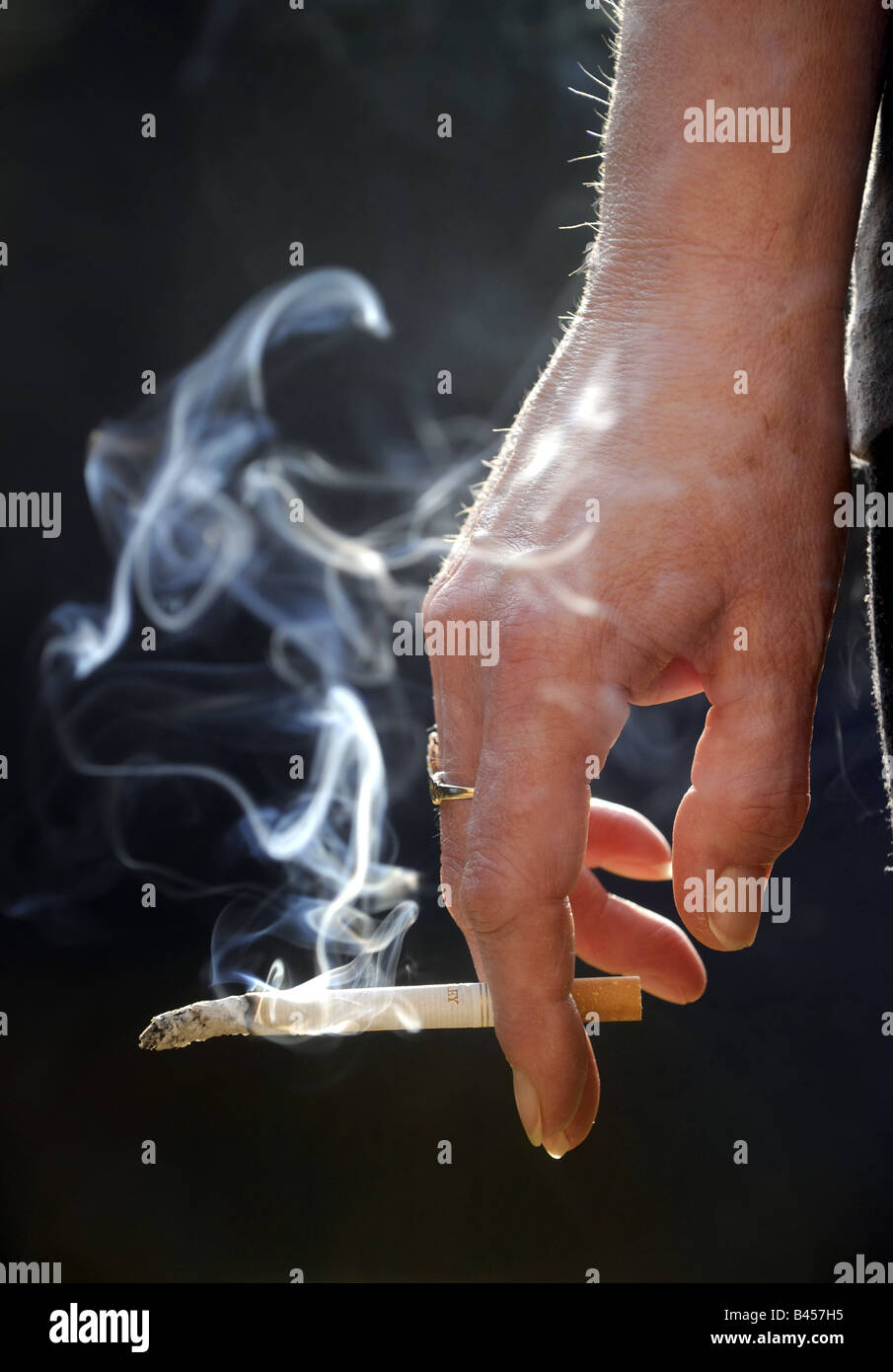 Un acceso il fumo di sigaretta in una mano womans. RE la salute dei fumatori di cancro del polmone malattia polmoni ospedali lifestyle sano REGNO UNITO Foto Stock