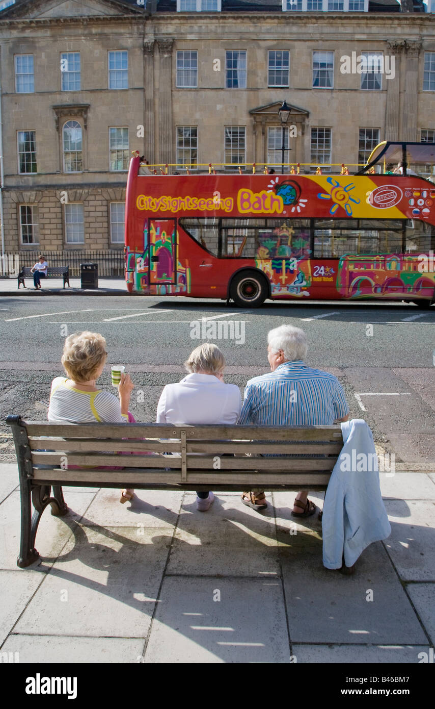Le persone aventi un tè picnic sulla panchina in street Bath Regno Unito con bagno bus panoramico Foto Stock