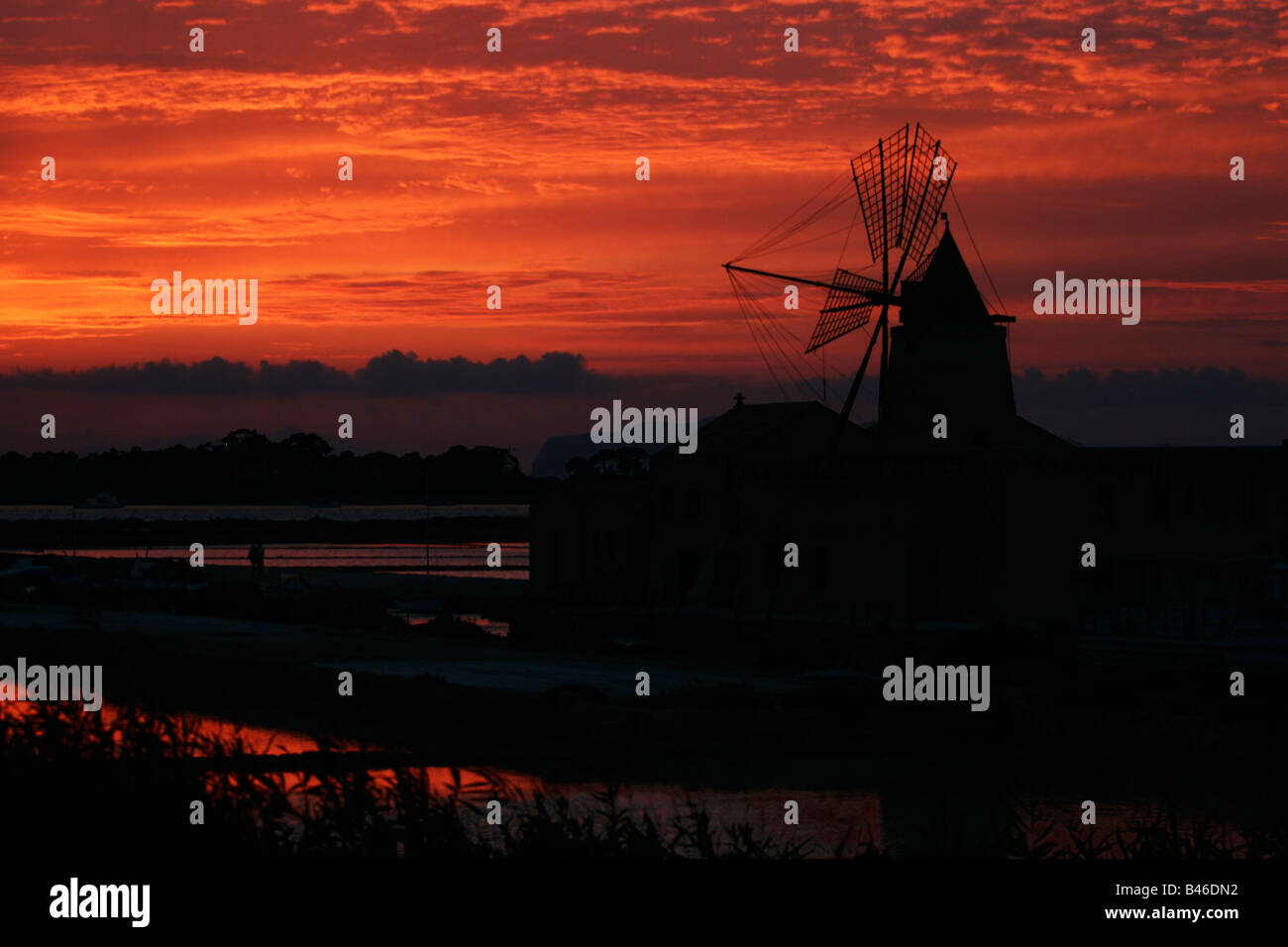 Rosso tramonto su mulini a vento utilizzati per produrre il sale di mare nella laguna di Stagnone da l'isola di Mozia , Marsala, Trapani Sicilia Foto Stock