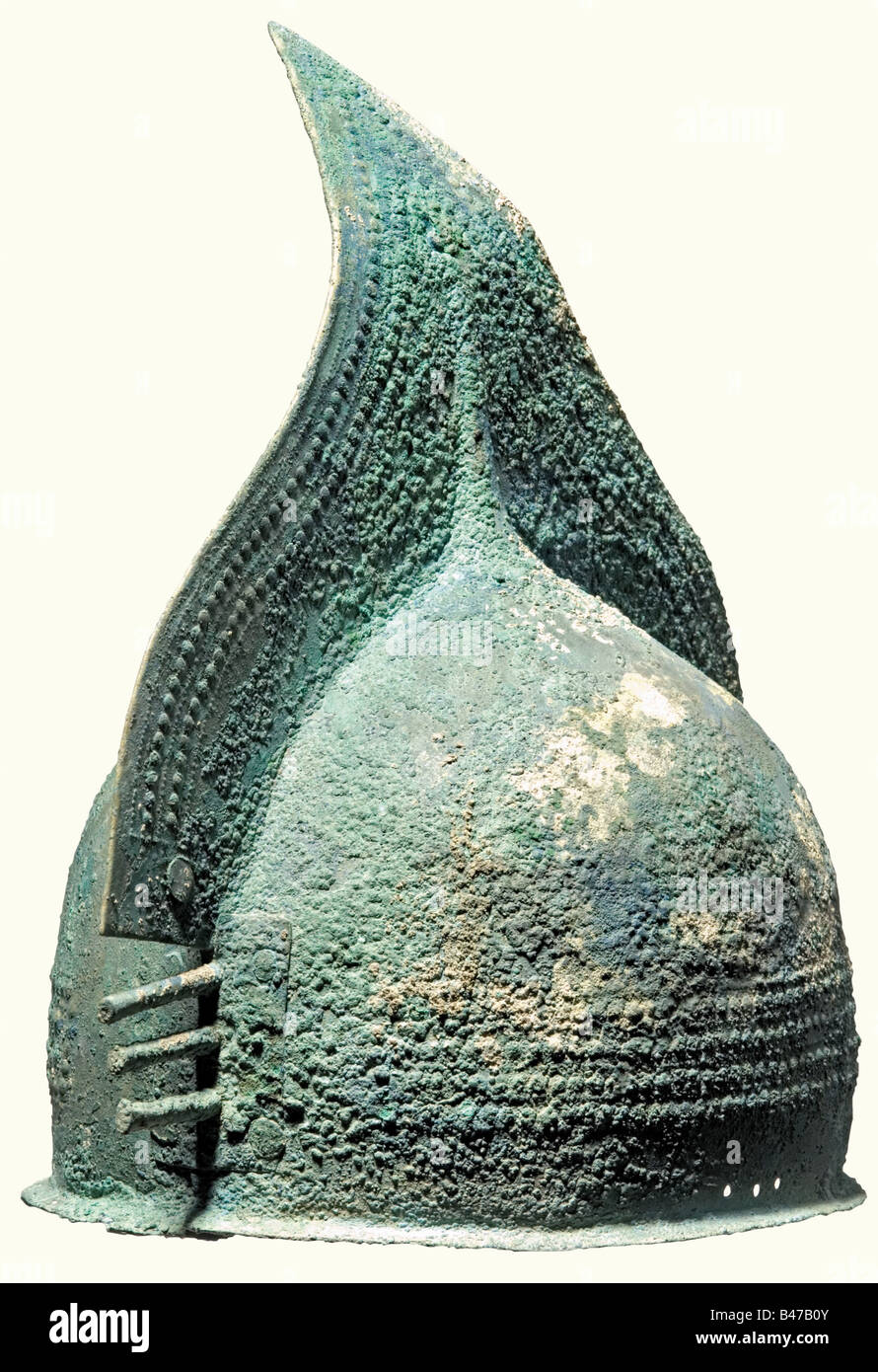 Un casco a pettine in bronzo, Early Iron Age, 9th/8th secolo a.C. un casco in bronzo composto da due piastre con bordo inferiore stretto e protendente. Il punto del pettine triangolare grande è leggermente piegato. Entrambe le metà del casco sono fissate insieme mediante bordi o rivettatura girati. I lati anteriore e posteriore del casco si sovrappongono e sono rivettati con pesanti piastre in bronzo, ciascuna decorata con un cerchio e ciascuna con tre punte sporgenti a forma di barra. Il corpo e il pettine del casco sono decorati con manopole grandi e piccole. Su ciascun lato sono presenti tre fori per il fissaggio del sottogola. Greeni, Foto Stock