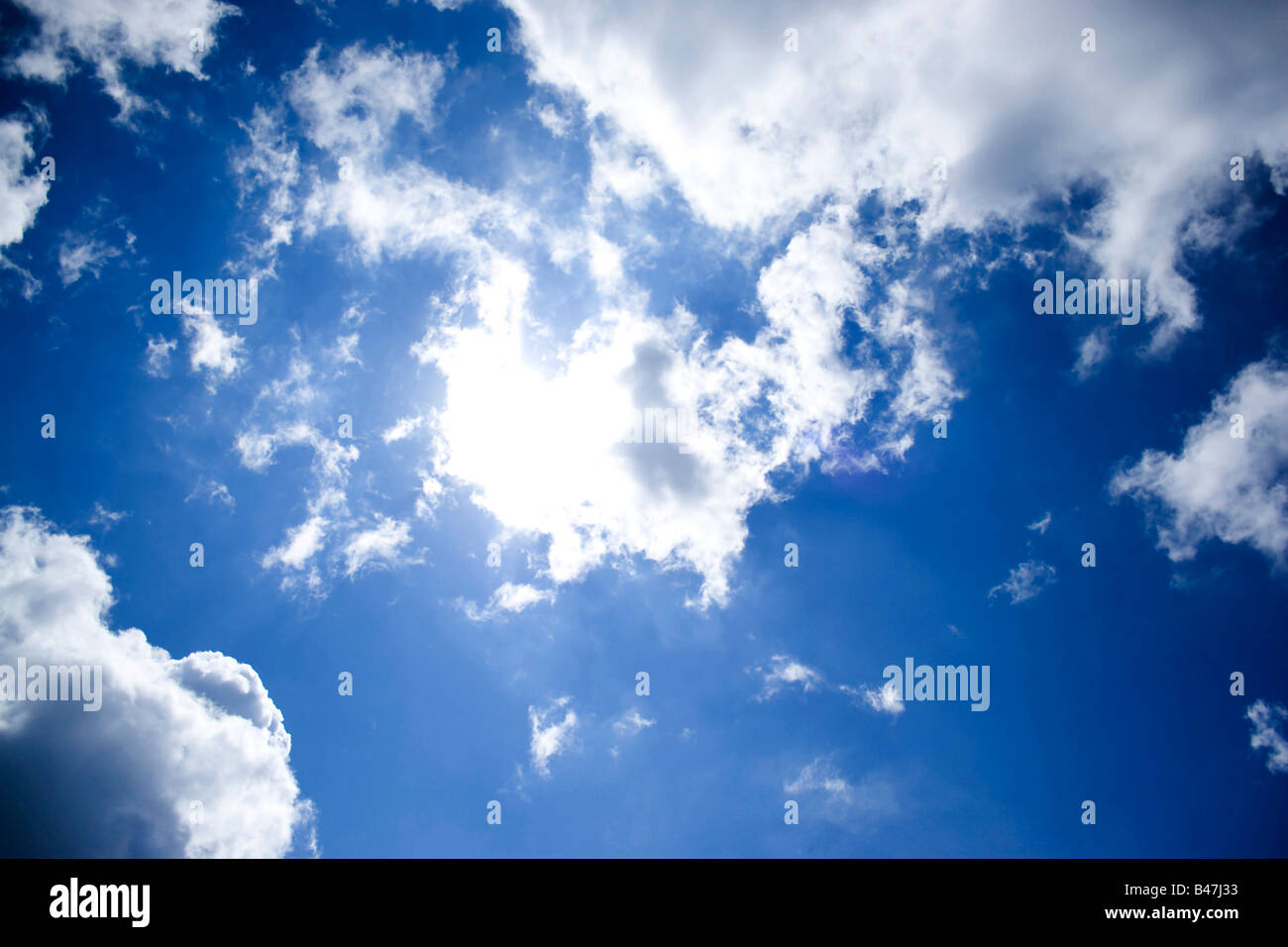 Un luminoso cielo blu e perfetta cotonosi nuvole con il sole cercando di brillare attraverso Foto Stock