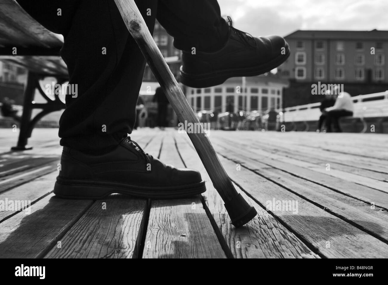 Uomo anziano con il bastone da passeggio seduta su una panchina su un molo Foto Stock