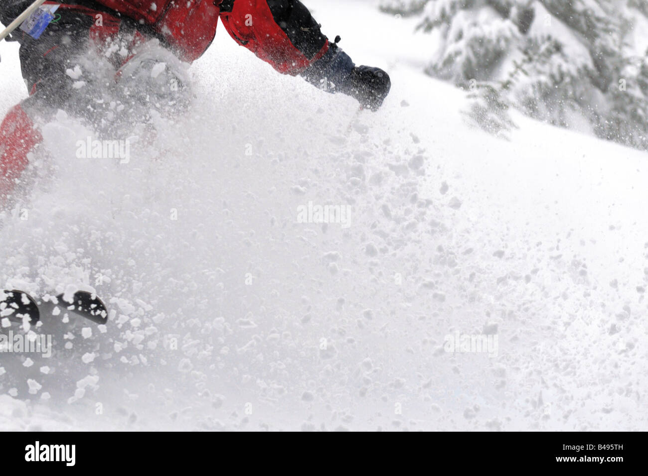 Un close-up di uno sciatore salta durante la sciata in polvere con un grande spruzzo di neve. Foto Stock