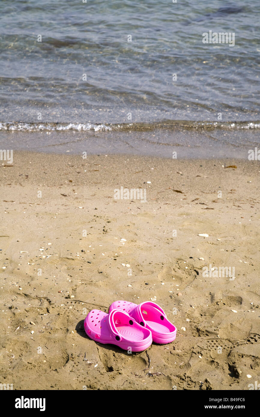 Una coppia di rosa luminoso scarpe lasciato dal bordo delle acque sulla sabbia Foto Stock
