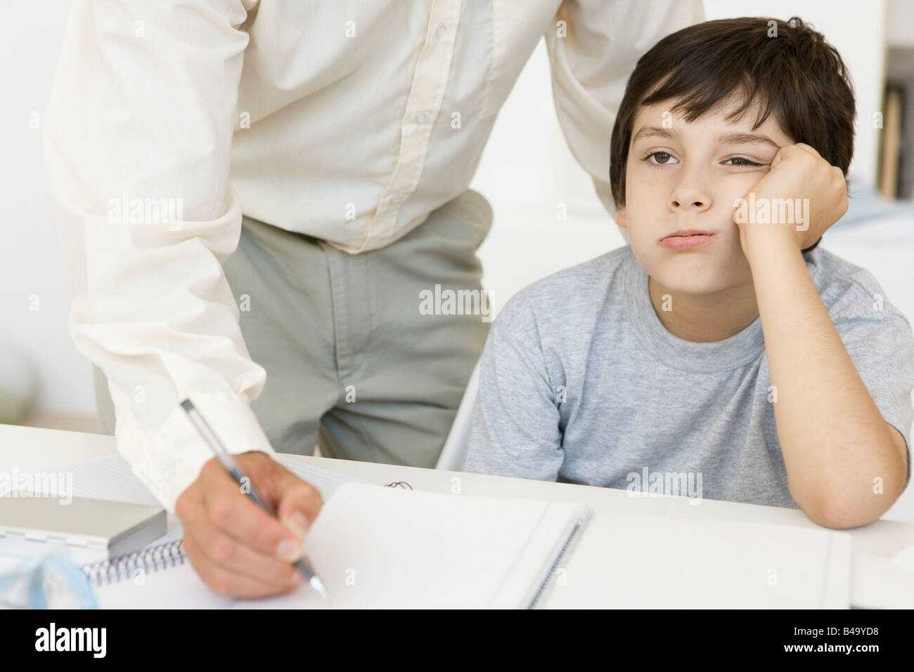 Padre aiutando figlio con i compiti, ragazzo tenendo la testa e lo sguardo lontano, vista ritagliata Foto Stock