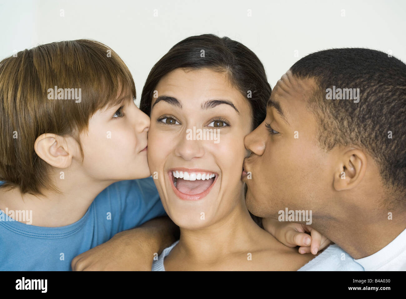 Donna sorridente alla telecamera come marito e figlio baciarla guance Foto Stock