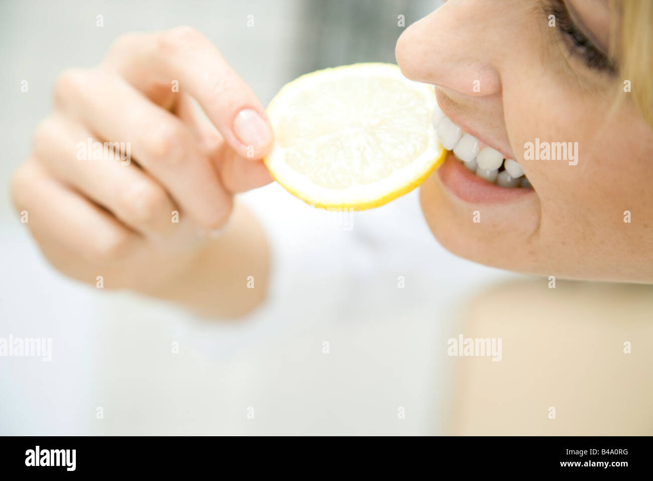 Donna di mordere nella fetta di limone, sorridente, close up Foto Stock