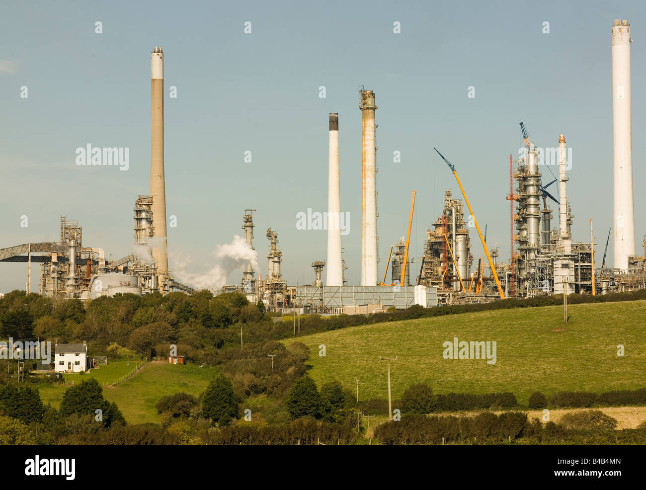 Piccolo agriturismo si accoccola sotto una grande raffineria di petrolio Foto Stock