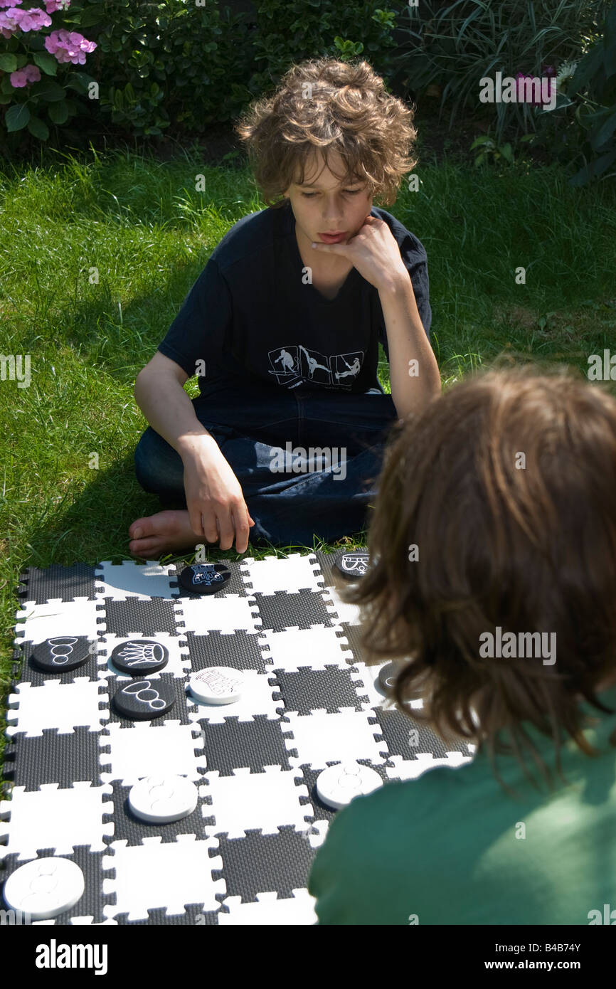 Due ragazzi seduti sul prato di un giardino a giocare a scacchi su una scacchiera enormi Foto Stock