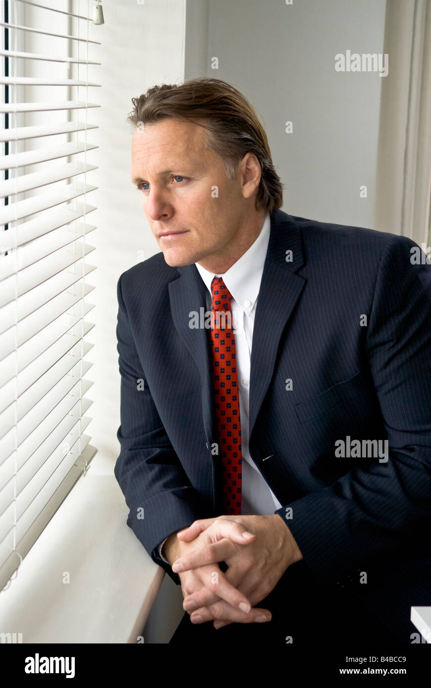 Un grave alla ricerca di imprenditore guarda fuori attraverso la sua finestra ofice Foto Stock