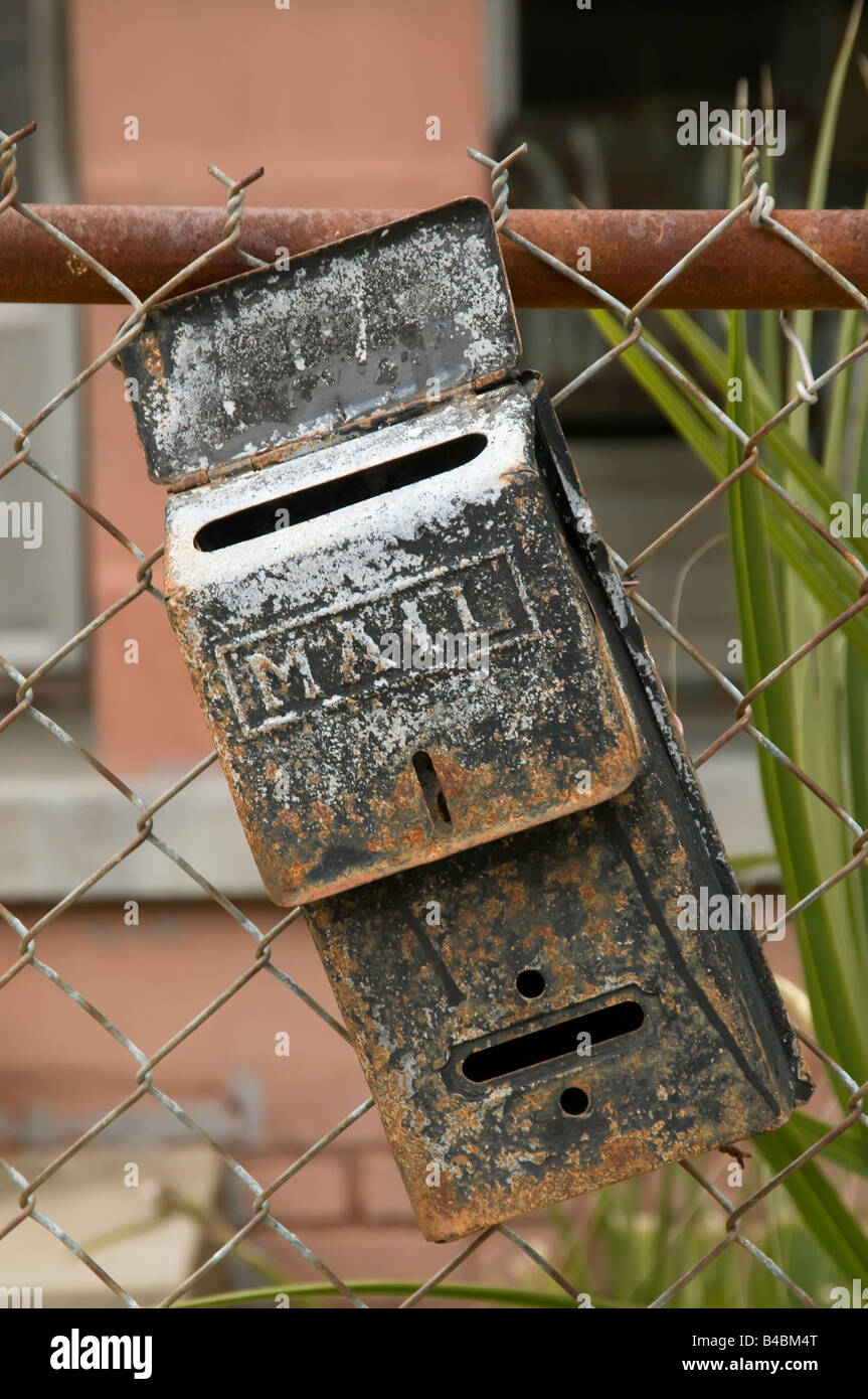 Piccola cassetta postale vintage cockeyed appeso sulla rete di recinzione a maglie nella parte anteriore della casa Foto Stock