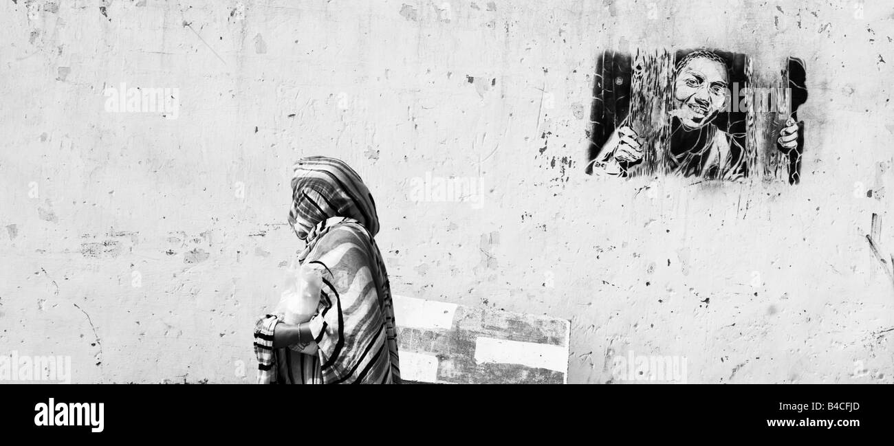Una donna musulmana passeggiate passato un muro dipinto in Mirleft, Marocco. Foto Stock