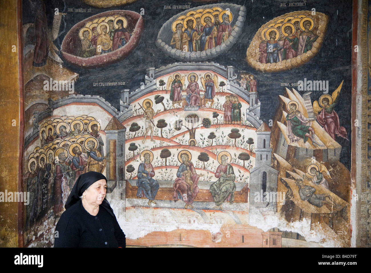 Vecchia donna con pittura religiosa sul muro fuori della chiesa nel 14 ° secolo monastero fortificato. Cozia Transilvania Romania Europa Foto Stock