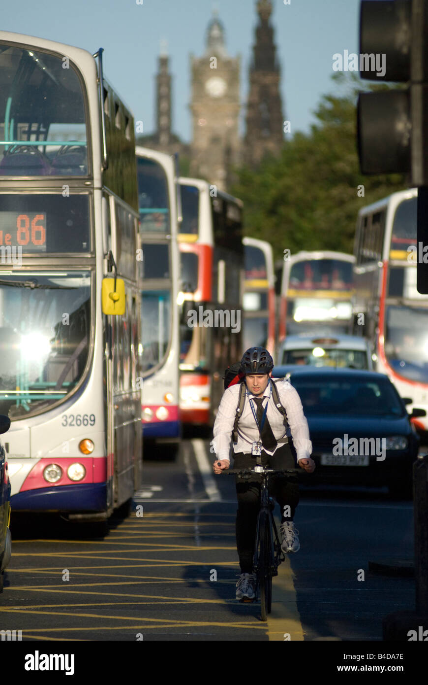 Un ciclista in bicicletta lungo Edinburgh Princes Street con molti autobus dietro di lui Foto Stock